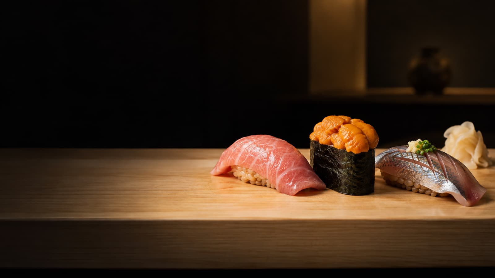 Illustration: O-toro, sea urchin and sardine nigiri with small rice, set on a pale hinoki counter at a dark sushi bar