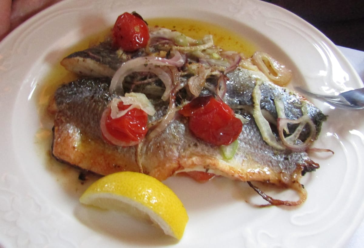 Pan-fried sea bass fillets with a lemon wedge, tomato and red onion